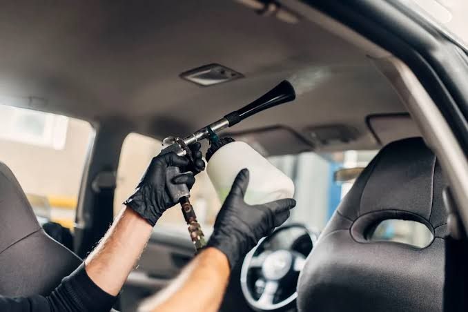 Technician foam-cleaning a car headliner where smoke residue settles